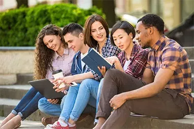 group of students sitting with books and a laptop on a college campus